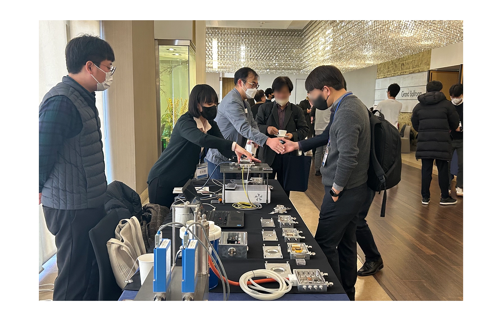 Employee giving explanations, people listening and people shaking hands in the back at The 18th Busan Dielectric Symposium