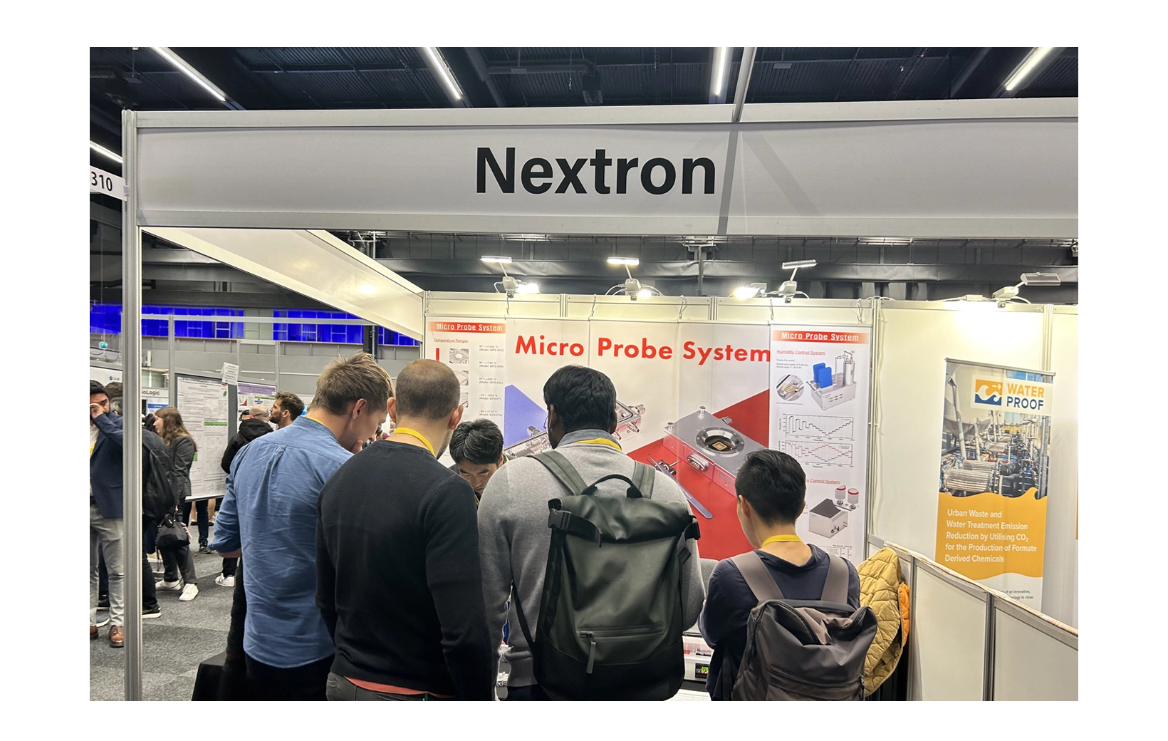 Research director giving an explanation to people gathered at Nextron's promotional booth at the 2023 ECS